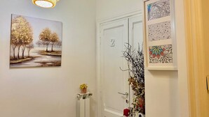A hallway with a white door marked "2", a radiator, a small plant, and a framed artwork depicting trees. - Domus Romana B & B (Rome)