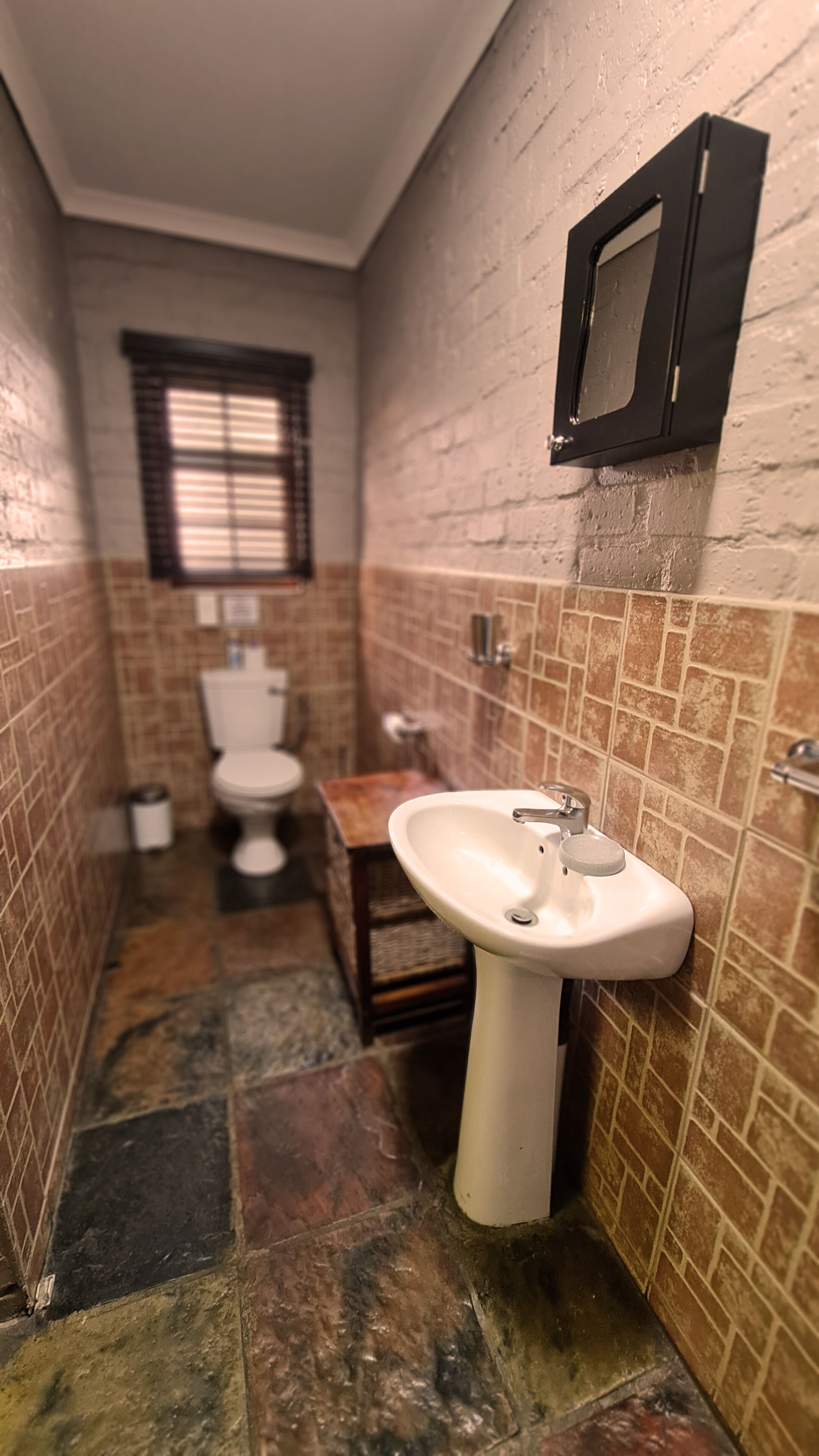 A bathroom with a white sink, a toilet, and a window with blinds.