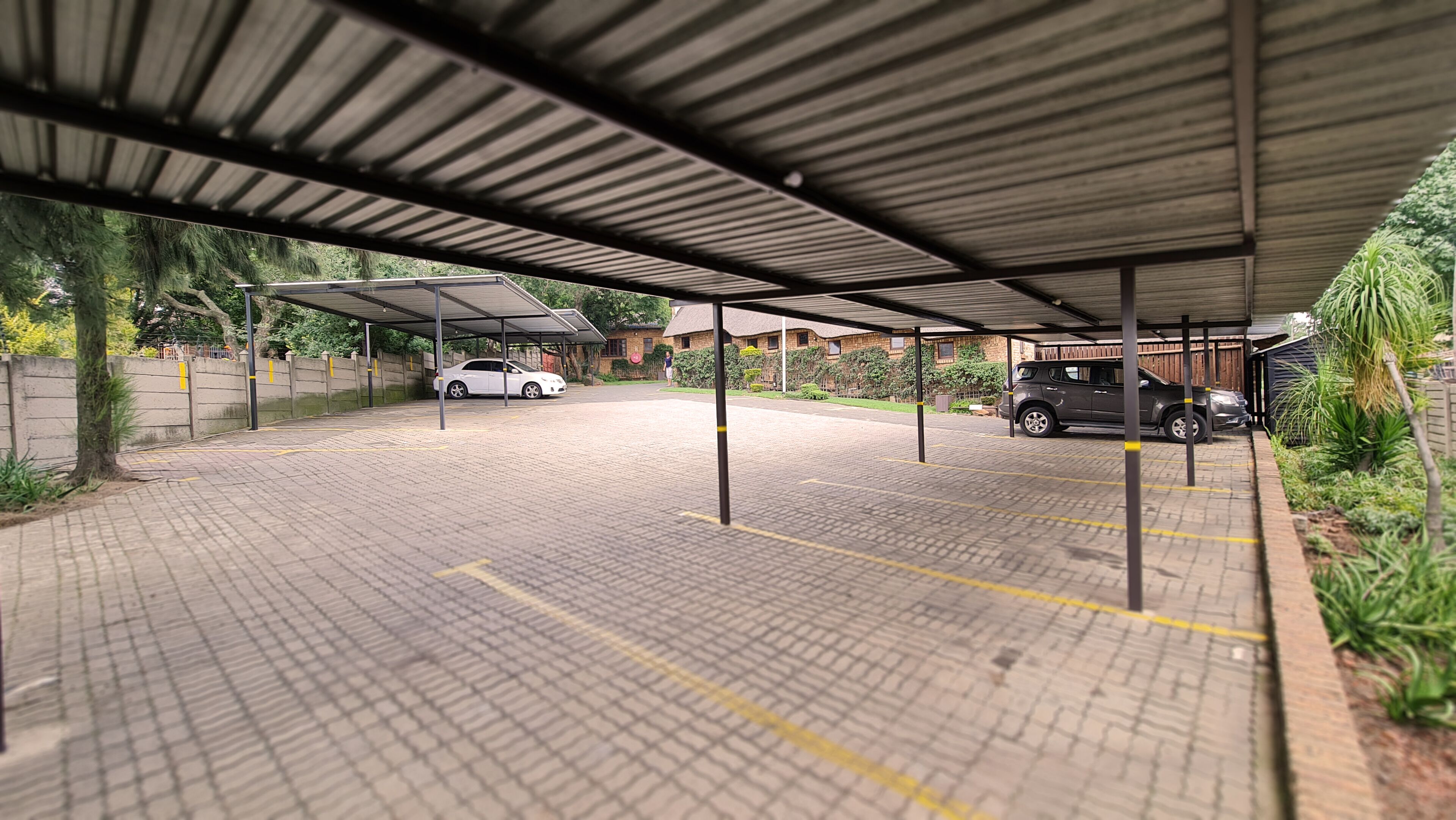 A covered parking area with a brick floor and a metal roof.