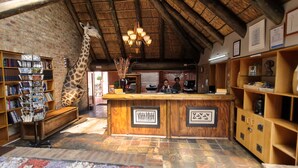 A reception area with a giraffe statue, wooden reception desk, and a brick wall. - Klein Bosveld Guesthouse (Emalahleni)