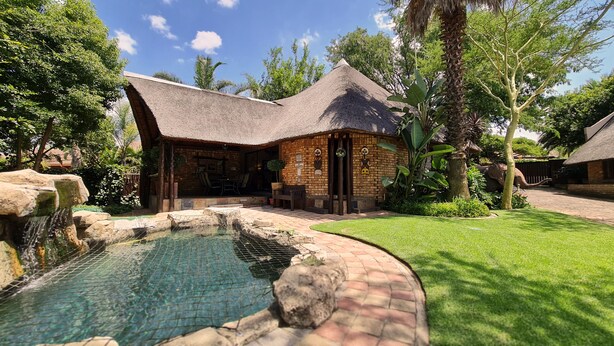 A thatched-roof building with a pool and a well-maintained garden. - Klein Bosveld Guesthouse (Emalahleni)