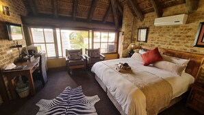 A spacious bedroom with a large bed, a zebra-patterned rug, a desk with a computer, and a window with blinds. - Klein Bosveld Guesthouse (Emalahleni)