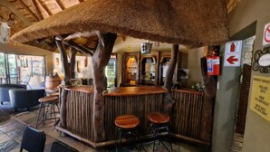 A rustic bar area with wooden stools and a thatched roof. - Klein Bosveld Guesthouse (Emalahleni)