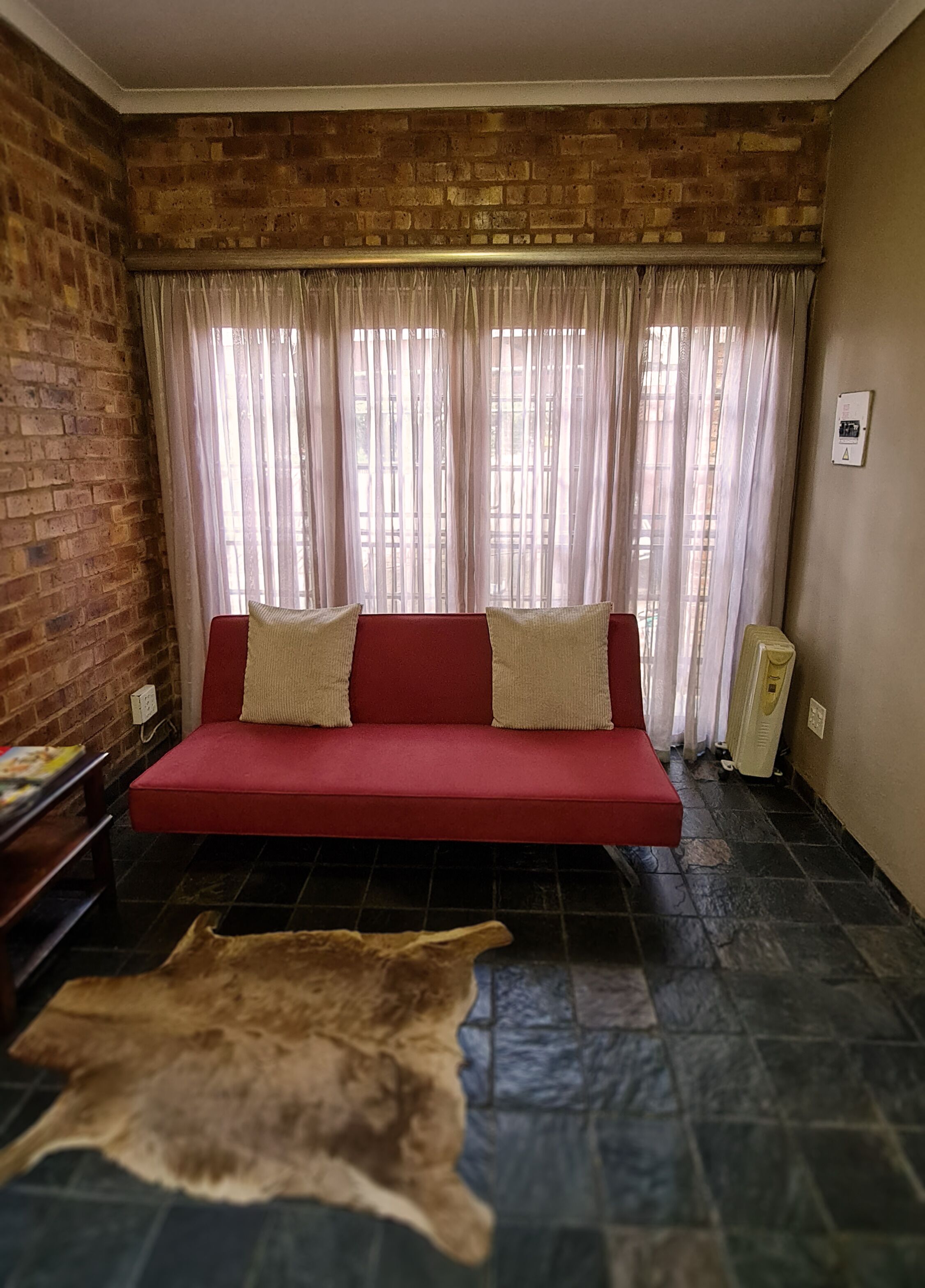 Una habitación con un sofá rojo, una pared de ladrillo y una alfombra de piel.