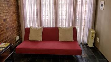 Una habitación con un sofá rojo, una pared de ladrillo y una alfombra de piel.