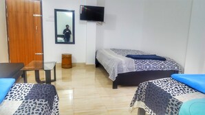 A room with a bed, a chair, a small table, a mirror, and a television on the wall.