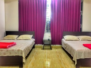 A room with two beds, each with a pillow and a red blanket. There is a window with a view of a building outside.