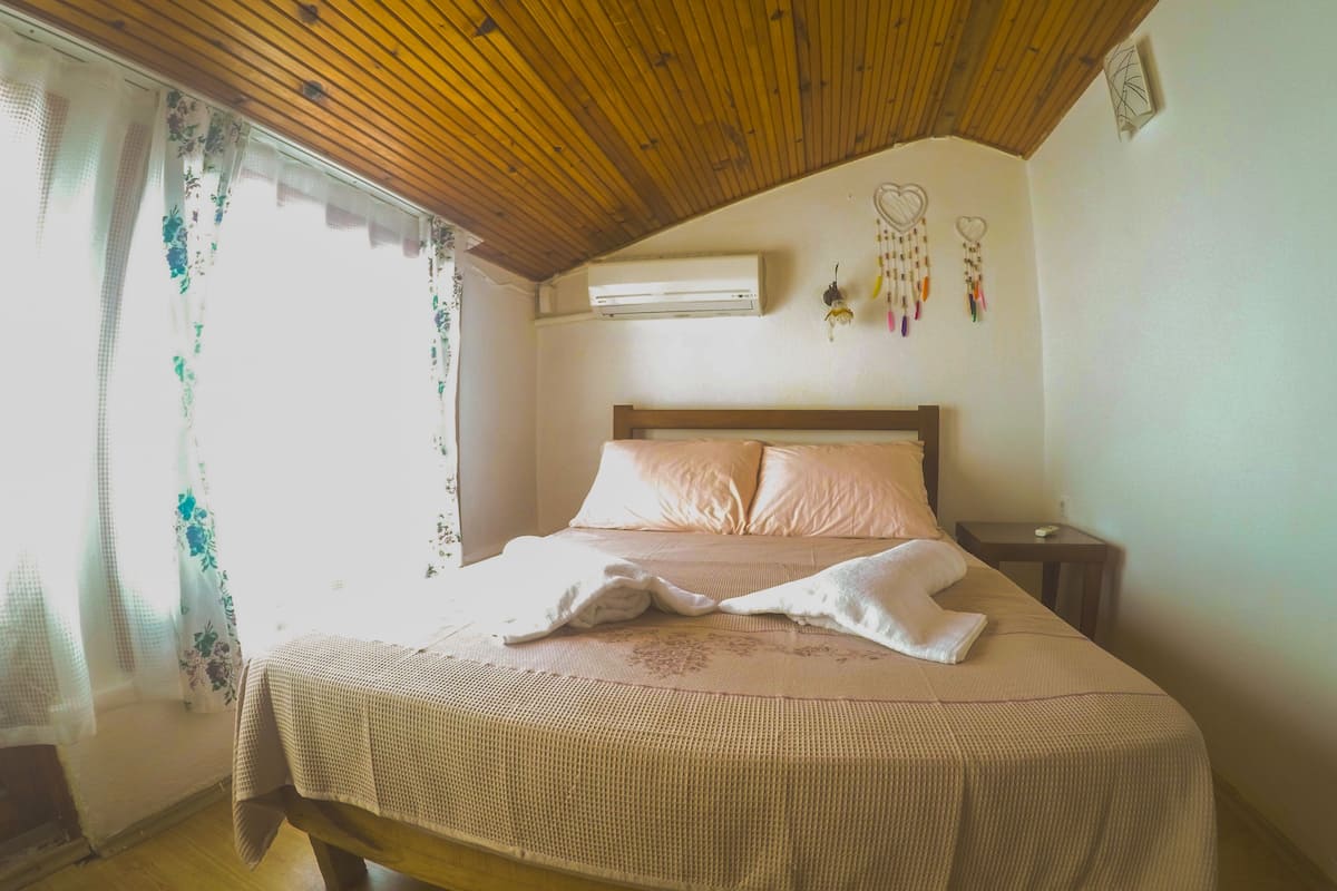 Un dormitorio con techo de madera, una cama con colcha rosa, una mesita de noche y un aire acondicionado de pared.