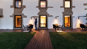 Een modern gebouw met raam- en deuropeningen met stenen omlijsting, een houten terras en buiten zitplaatsen.