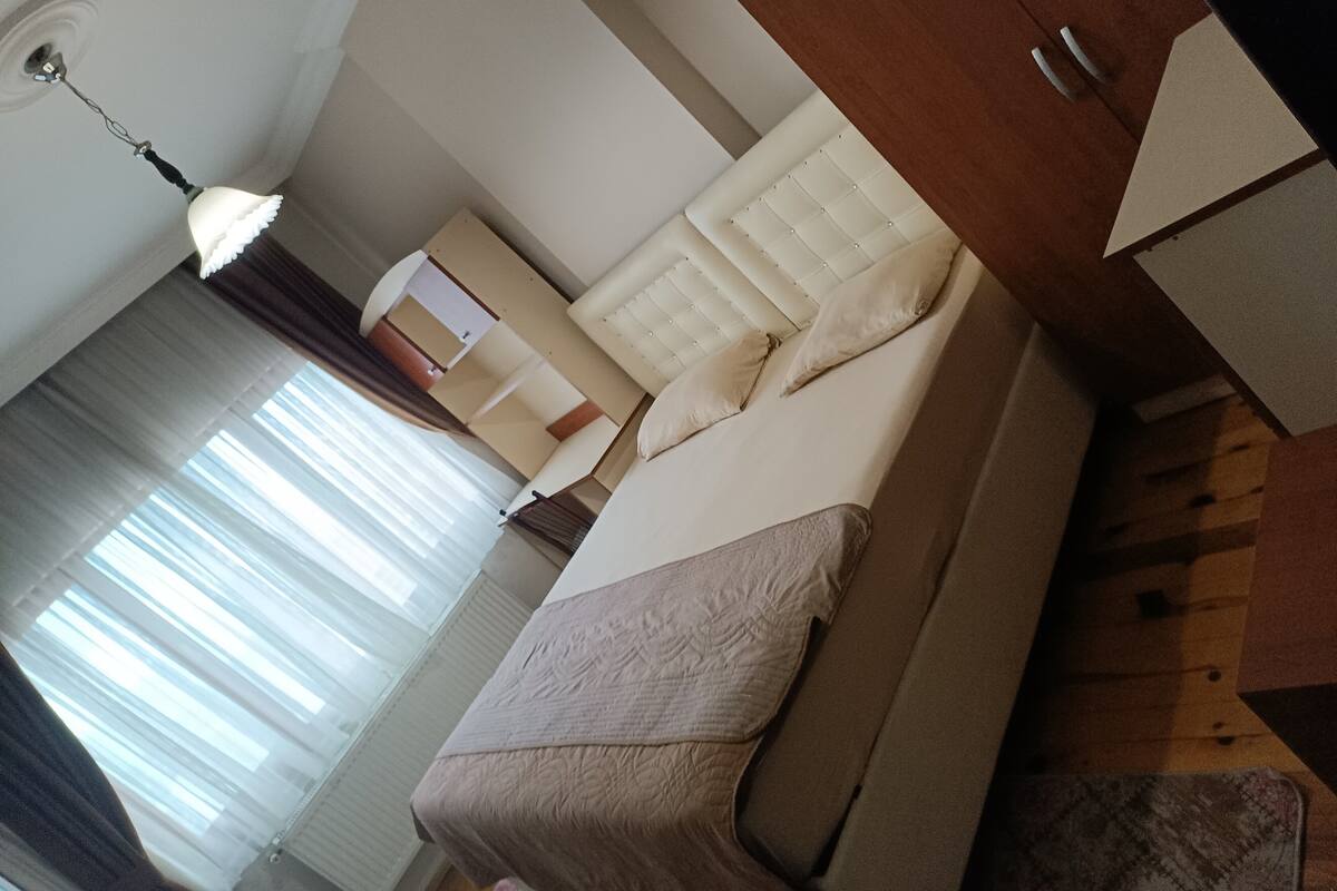 A modern hotel room with a bed, a bedside table, a lamp, and a window with curtains.