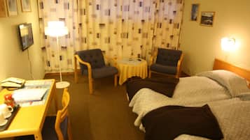 Una camera d'albergo con un letto, due poltrone, un tavolino rotondo e una scrivania con lampada e telefono.