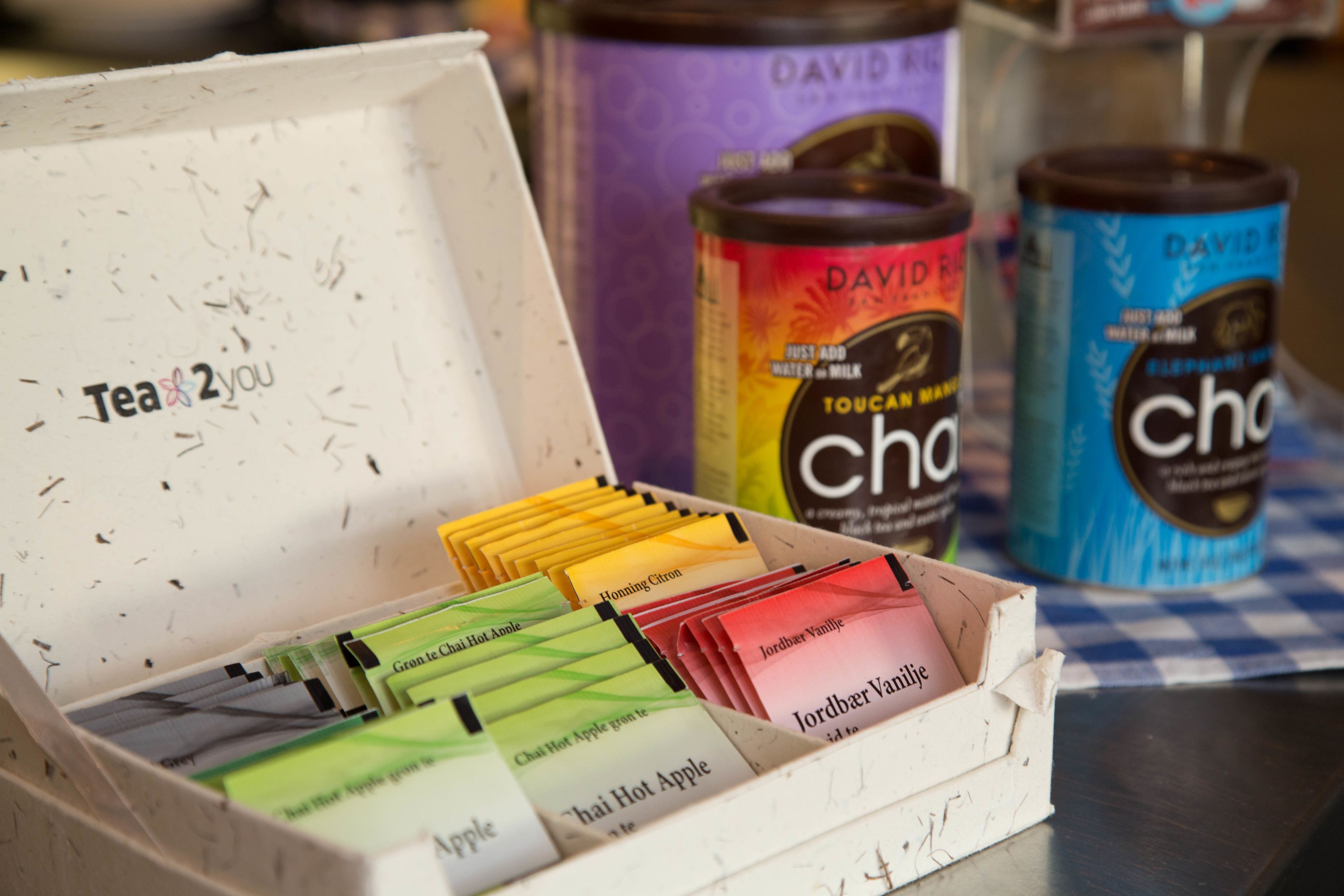 A box of tea bags with labels like "Honning Citron" and "Jordber Vanilla" next to two cans of David's brand tea.