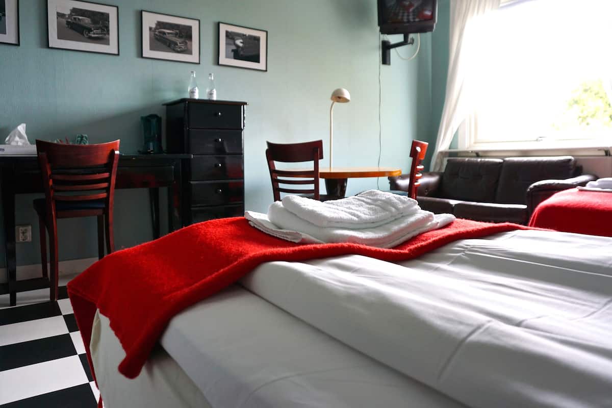 A hotel room with a bed, a desk, a chair, a lamp, and a window.