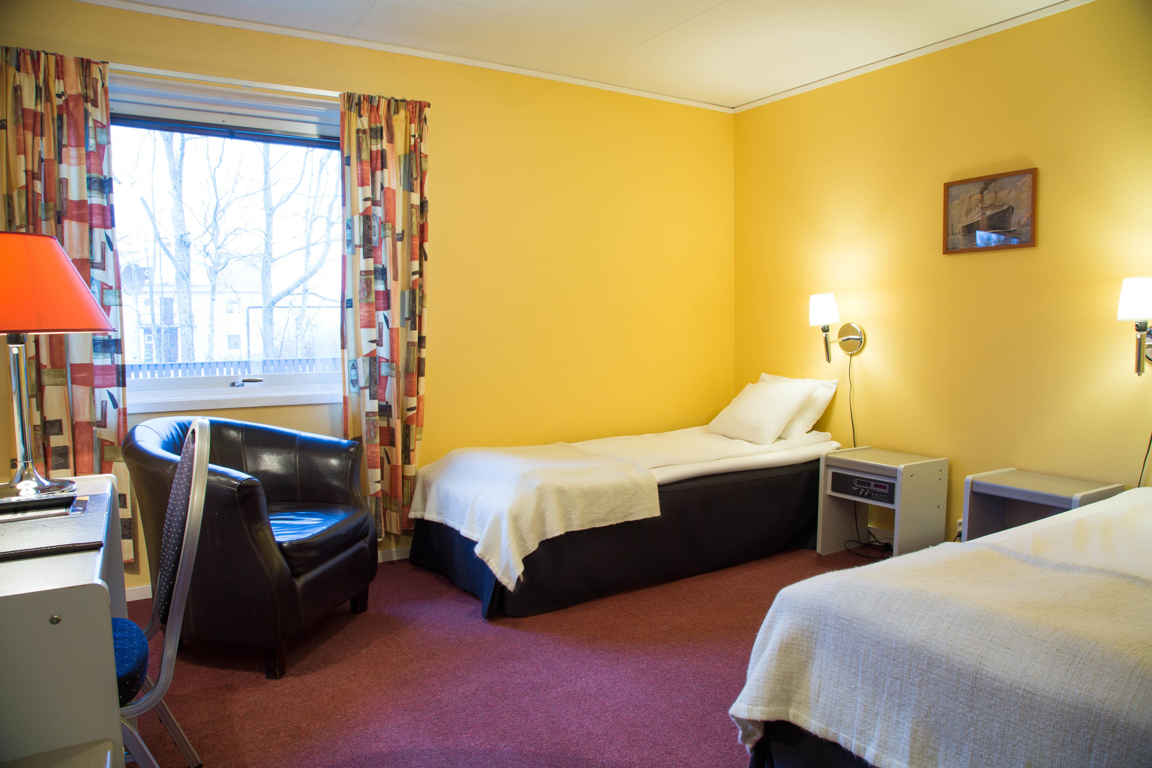 Une chambre d’hôtel avec un lit, une chaise, un bureau et une fenêtre avec des rideaux.