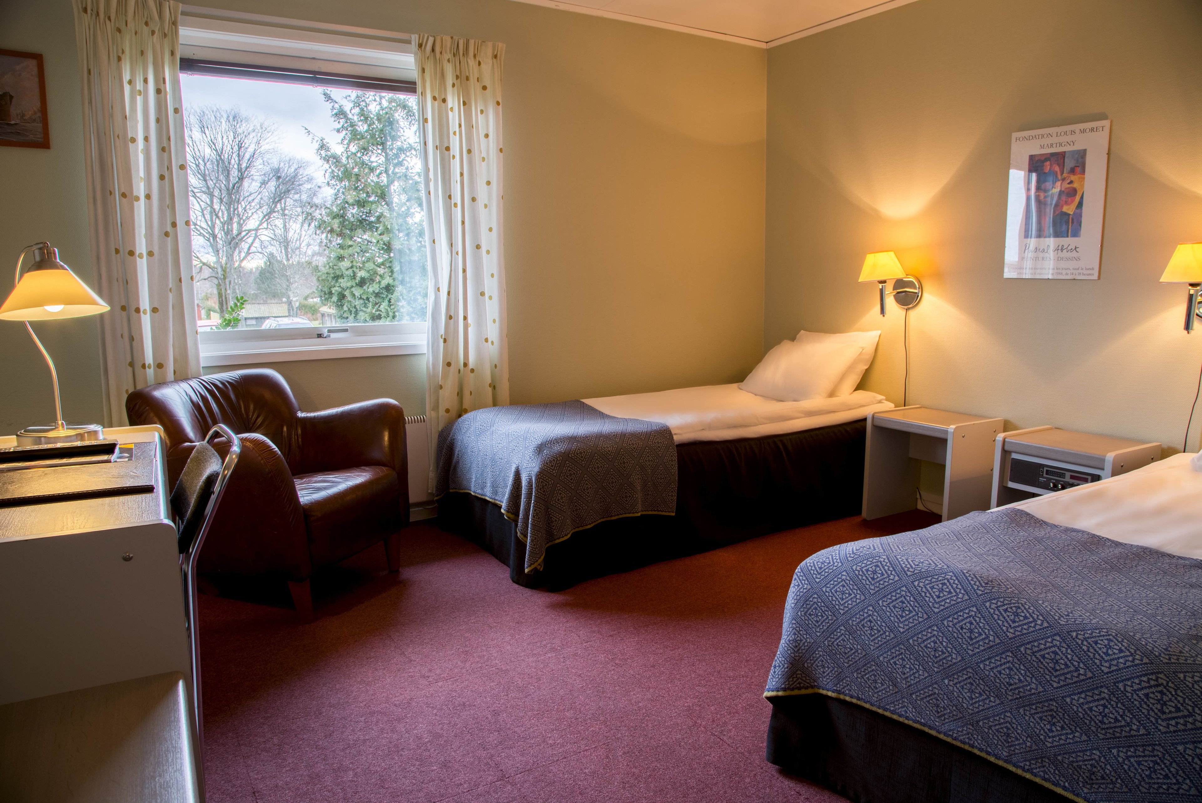 Een hotelkamer met twee bedden, een bureau, een stoel en een raam met gordijnen.