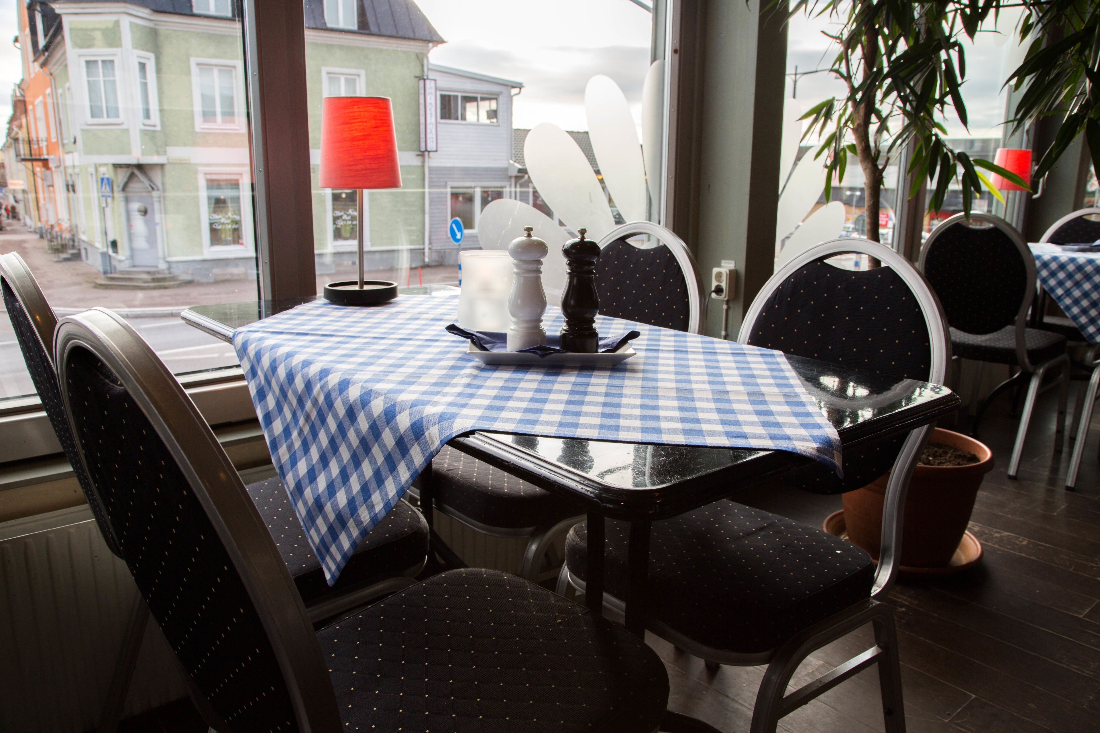 A restaurant with a checkered tablecloth, black upholstered chairs, and a red lamp.