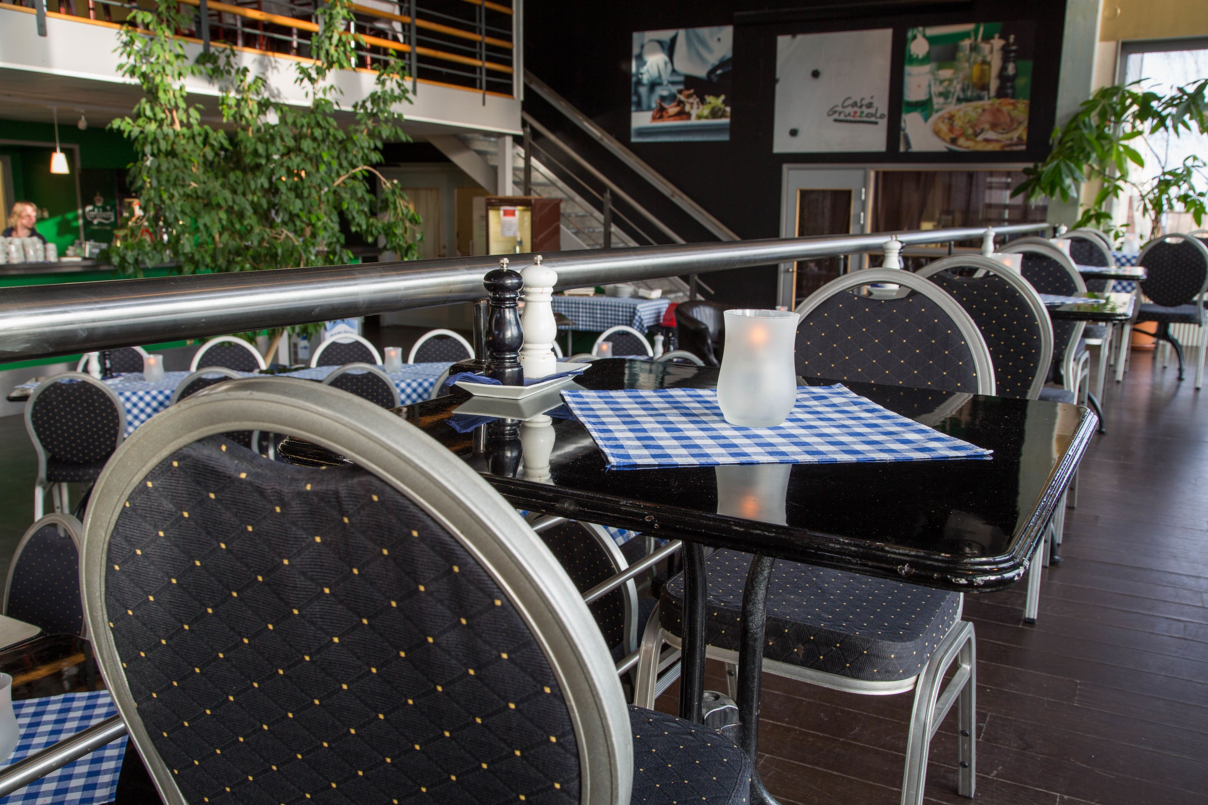 Un interior de restaurante con mesas redondas, sillas y una escalera de fondo.