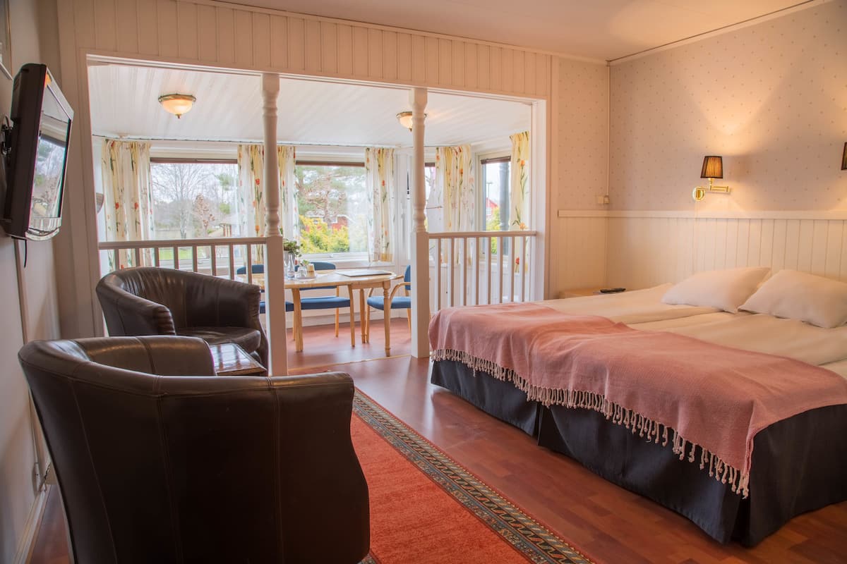 A bedroom with a large bed, a chair, a small table, and a view of the outdoors through a window.