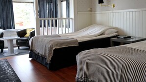 Quarto de hotel com duas camas, uma mesa pequena, uma cadeira e vista para o exterior.