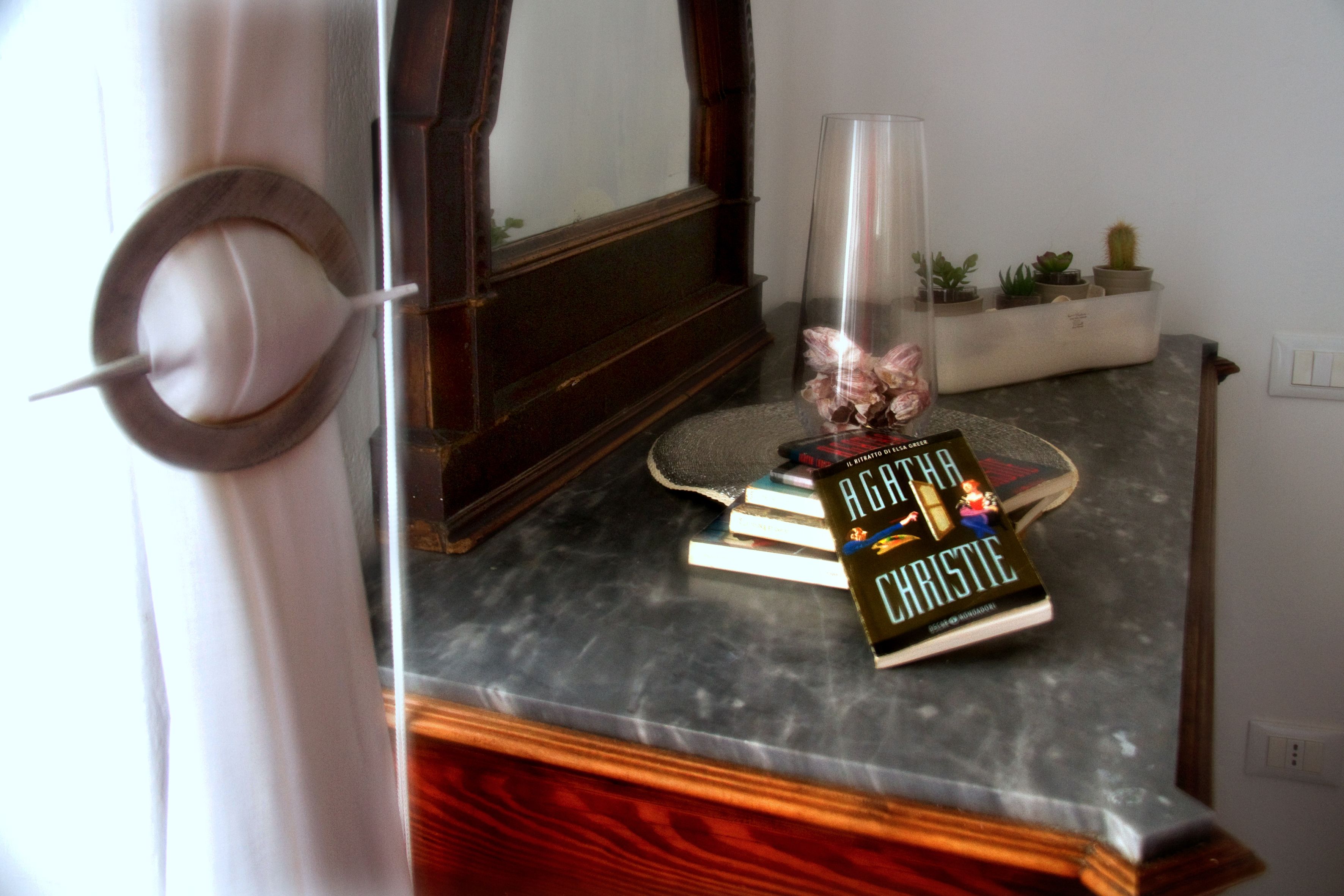 Una stanza con una scrivania in legno, uno specchio, un vaso con fiori e un libro intitolato 