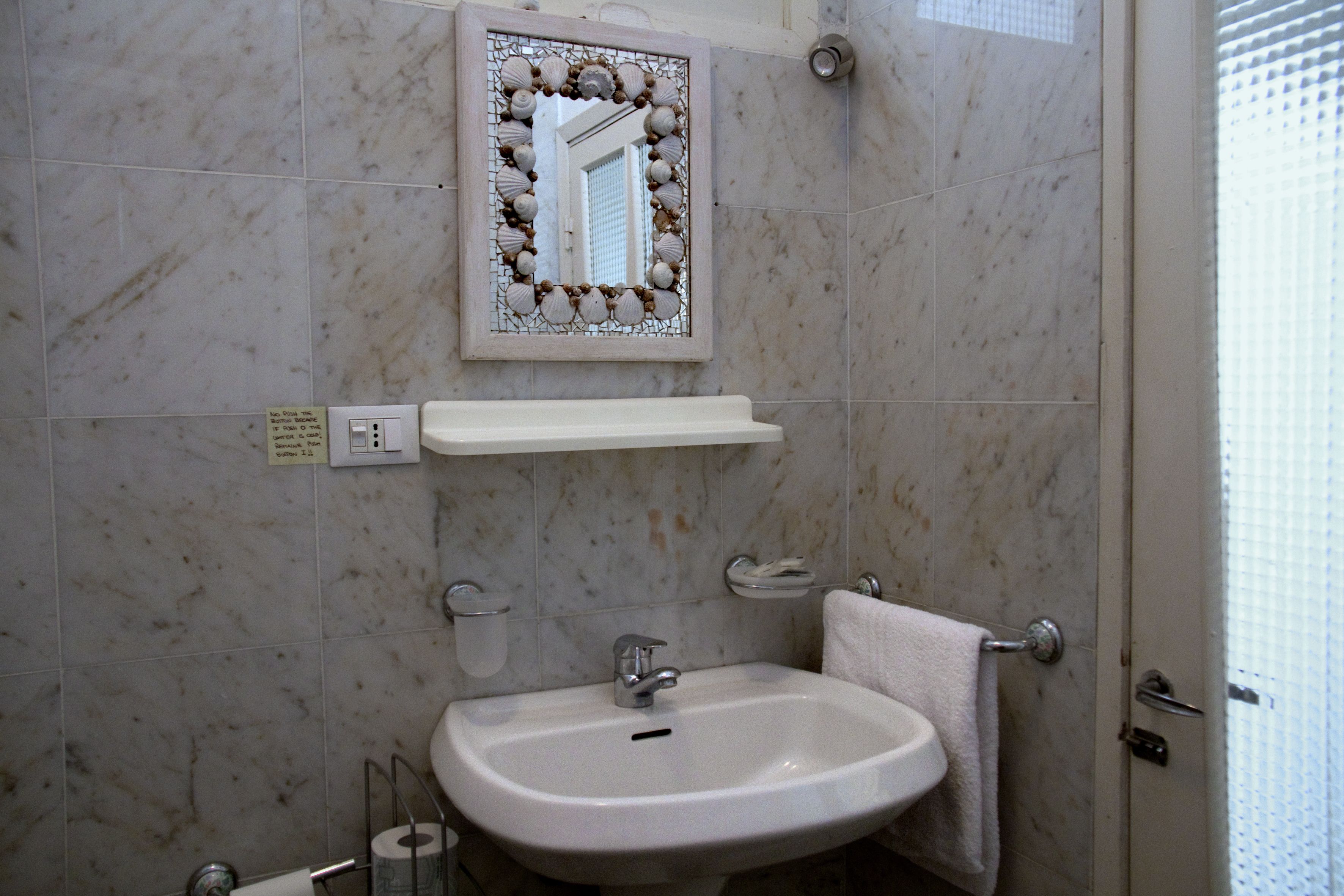 Ein Badezimmer mit Marmorfliesen, einem Waschbecken mit Spiegel darüber und einem Handtuch an der Wand.