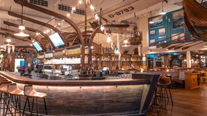 A bar area with wooden bar stools, a counter, and a hanging wooden boat decoration. - Europa-Park Erlebnis-Resort, Hotel Krønasår (Rust)