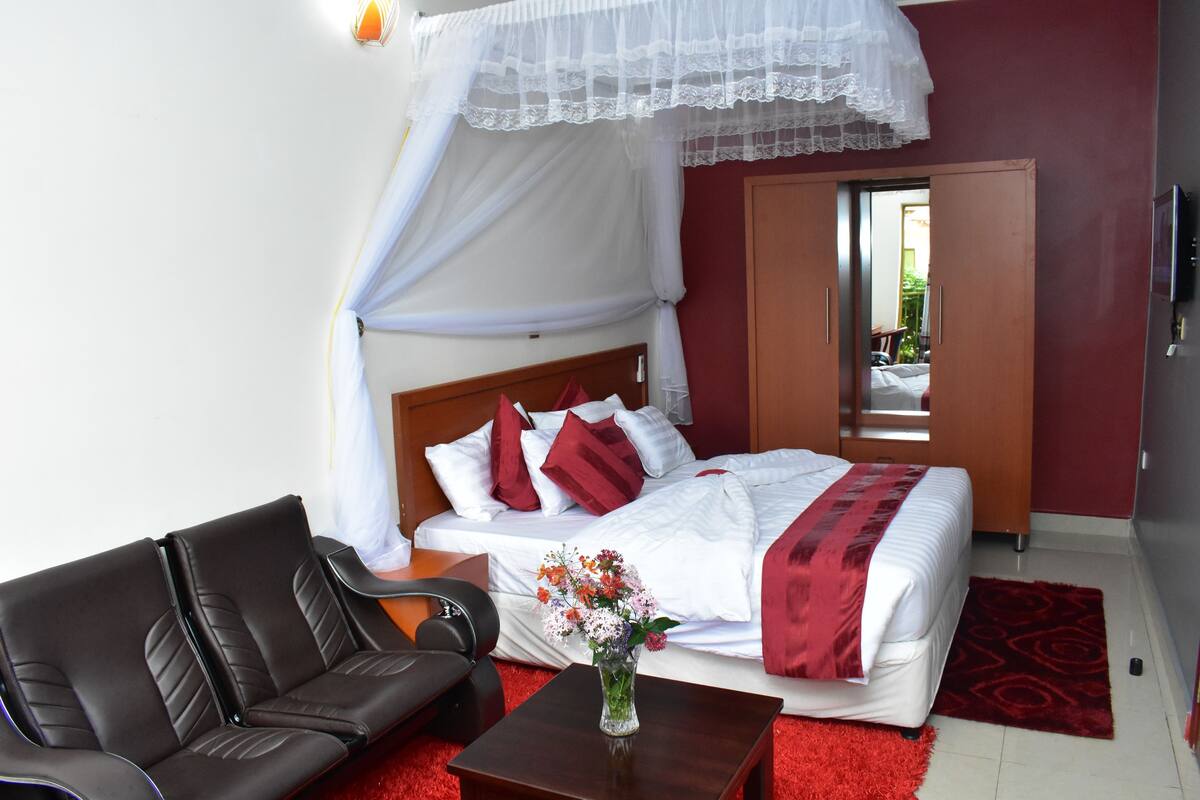 Una camera d'albergo con un letto, un divano, un tavolino con un vaso di fiori e un tappeto rosso.