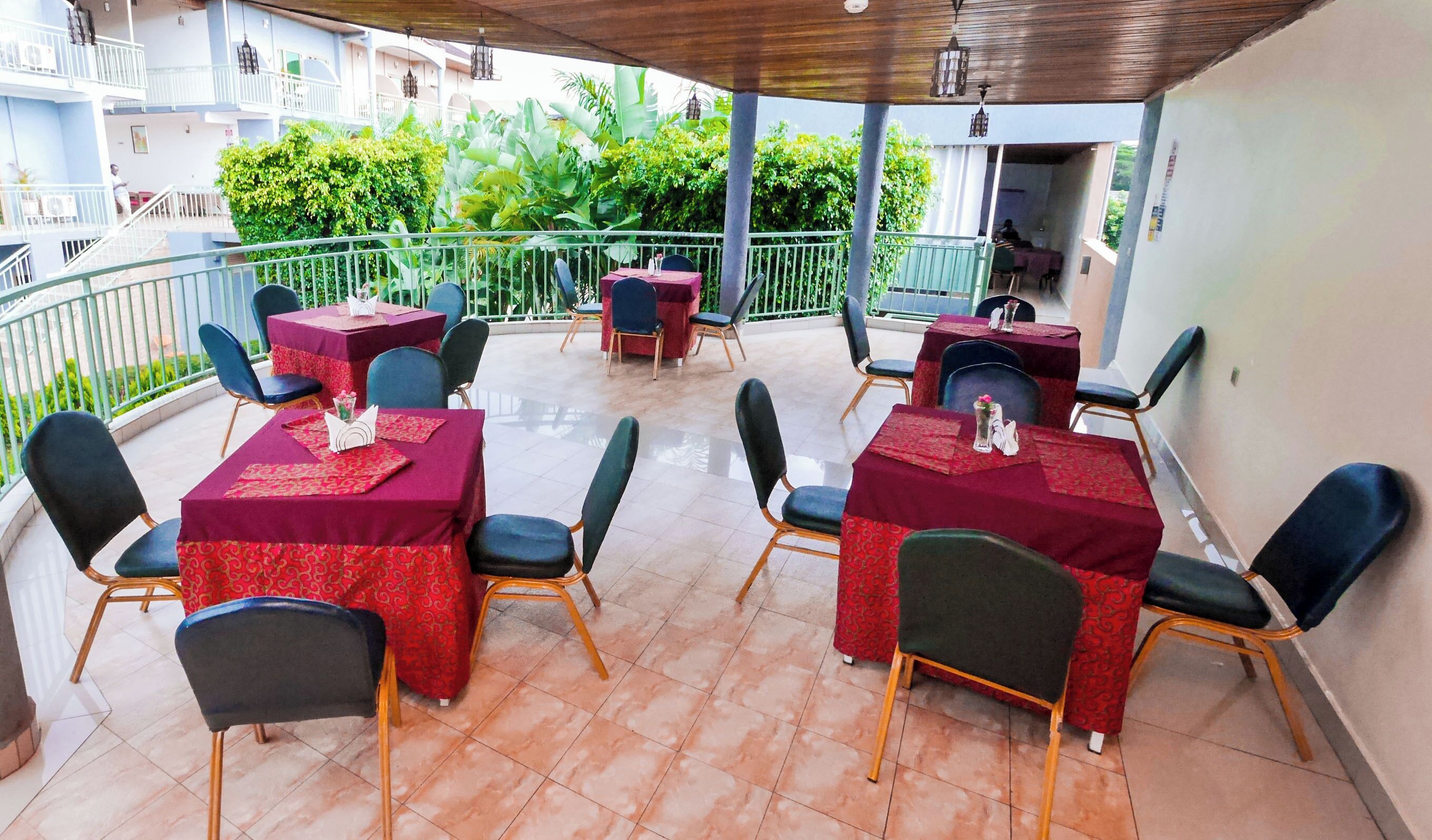 An outdoor terrace with tables and chairs, surrounded by greenery and a balcony.