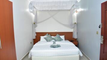 Una habitación de hotel con cama, cortinas blancas, cabecera de madera y mesita de noche.