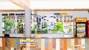 A bar area with shelves of liquor bottles, a sign warning about a slippery floor, and two bar stools. - Lebanon Hotel (Kigali)