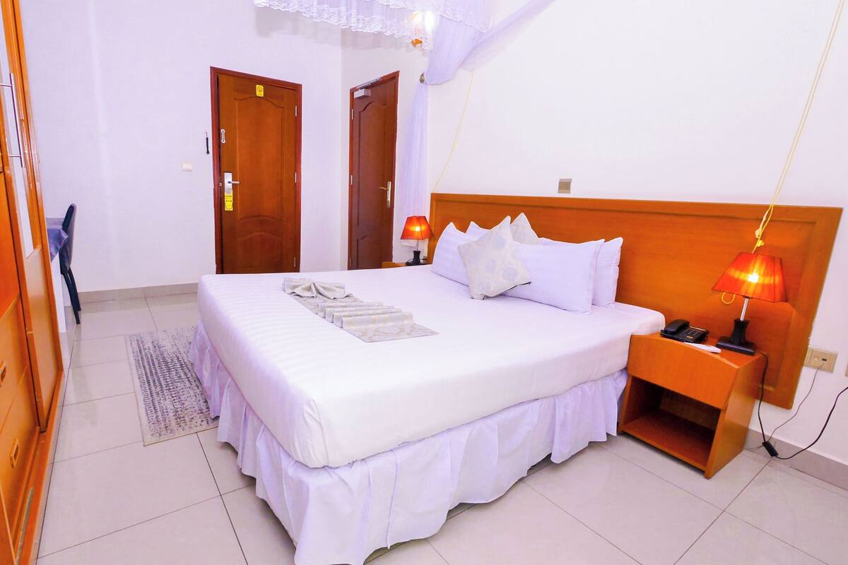 Una camera d'albergo ordinata, con un letto grande, un comodino con una lampada e un armadio.