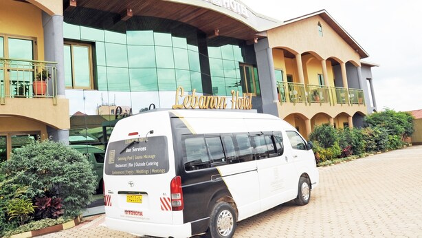 A white van parked in front of Lebanon Hotel with a sign listing services like swimming pool, sauna, and restaurant. - Lebanon Hotel (Kigali)