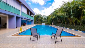 A swimming pool with two chairs, surrounded by lush greenery and a building with blue and purple walls. - Lebanon Hotel (Kigali)