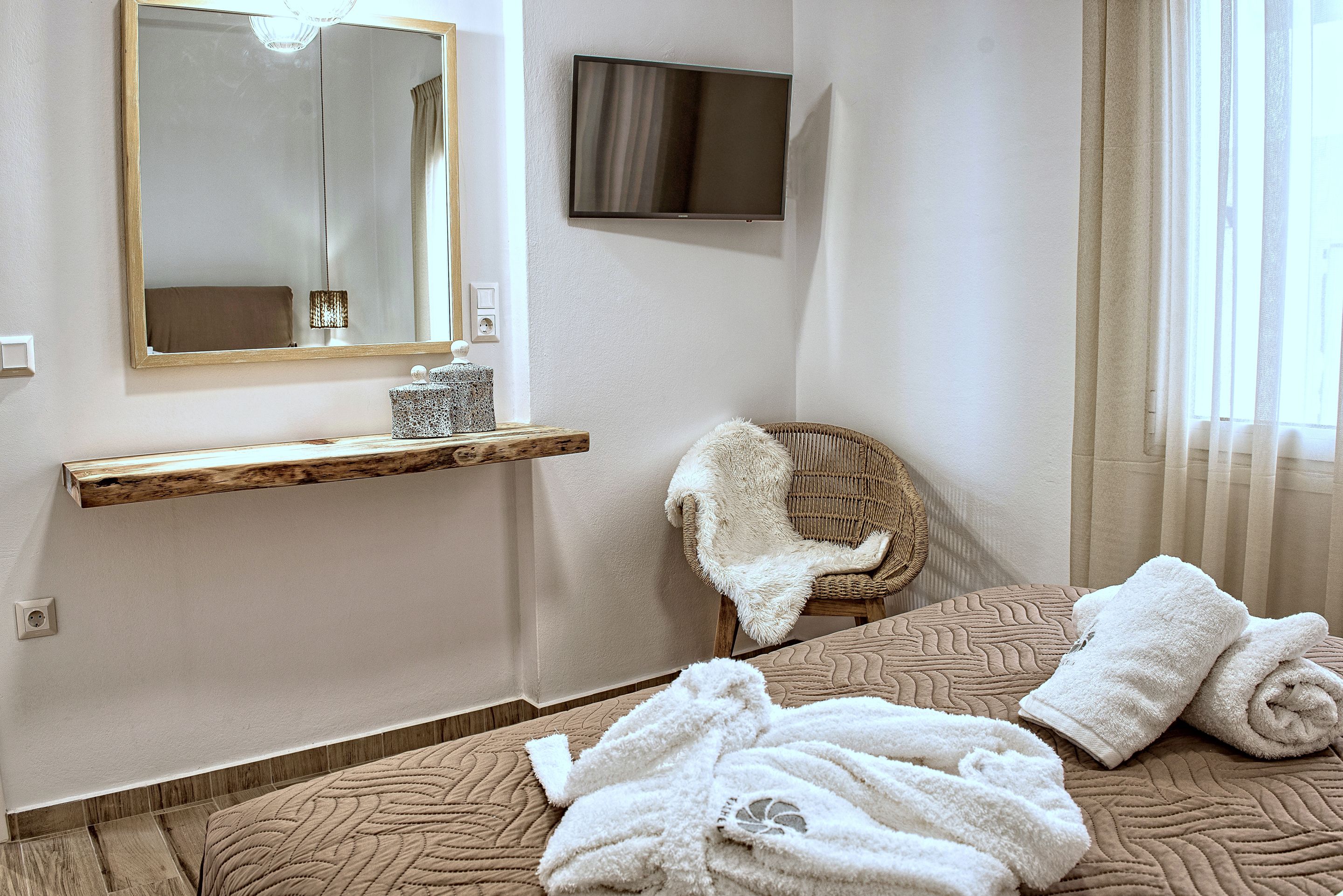 Ein Hotelzimmer mit einem Bett, einem Sessel, einem Fernseher, einem Spiegel und einem Regal mit Lampe und Dekoration.