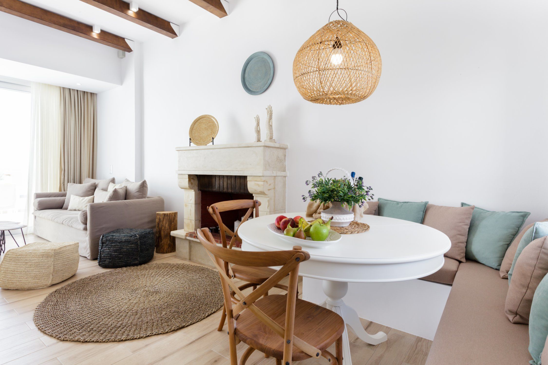 A modern living room with a white round table, a sofa, a wooden chair, a woven rug, and a hanging light fixture.