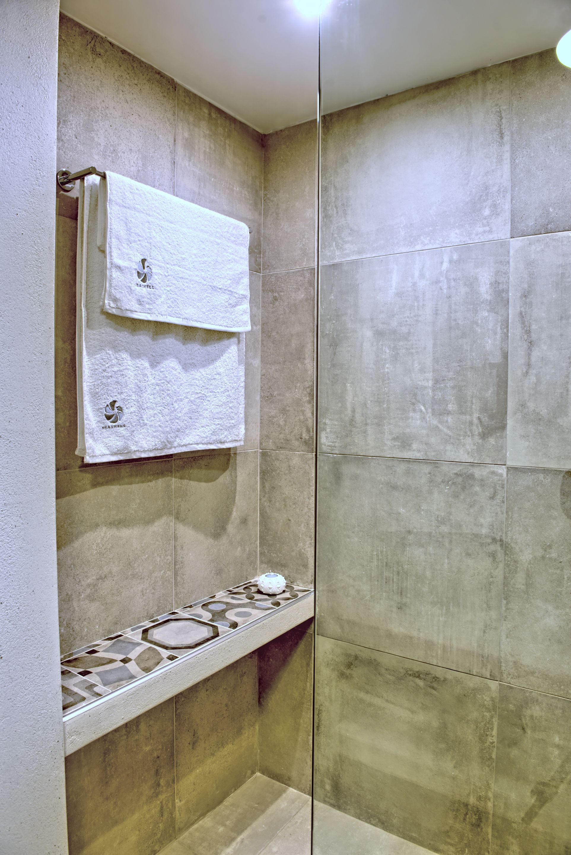 A bathroom with a glass shower enclosure, a towel rack with a towel, and a decorative tile border.