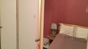 Een slaapkamer met een bed, nachtkastje, lamp en een wandairconditioner.