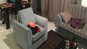 Een woonkamer met een grijze fauteuil, een bank, een salontafel met een vaas en een roos, en een eethoek met een tafel en stoelen.