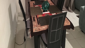 Een eetruimte met een tafel voor vier personen, een vaas met bloemen en een stoel met een bijzondere geweven zitting.