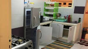 Een compacte keuken met een gasfornuis, een koelkast en een magnetron. Er is een klein aanrecht met een spoelbak en een raam erboven.