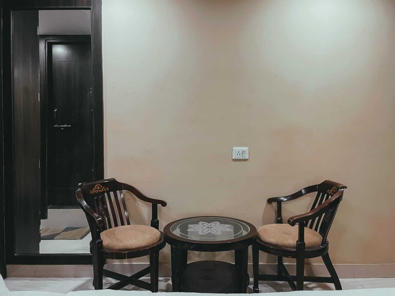Una habitación con dos sillas de madera y una pequeña mesa redonda, un enchufe en la pared y una puerta de madera oscura.