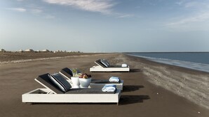 A beachside lounge area with sun loungers, a bowl of fruit, and a glass of water.