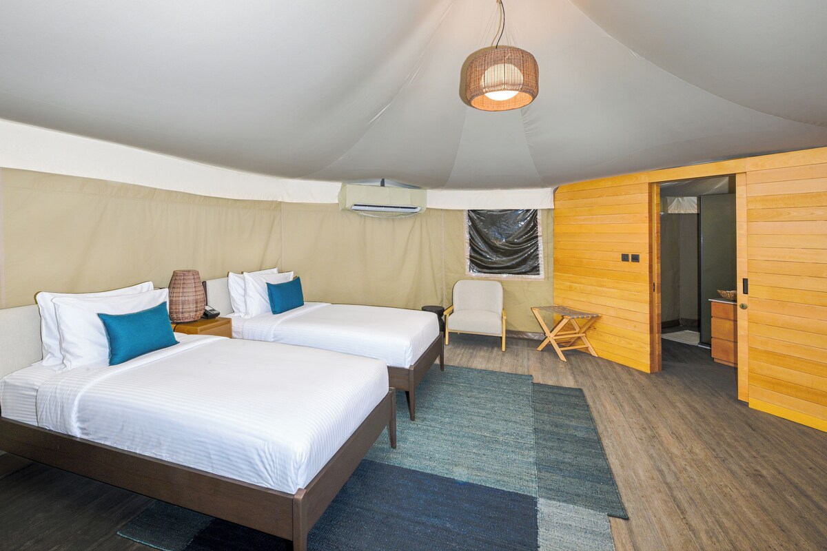 Habitación de hotel con dos camas, una mesita, una silla y un armario de madera.