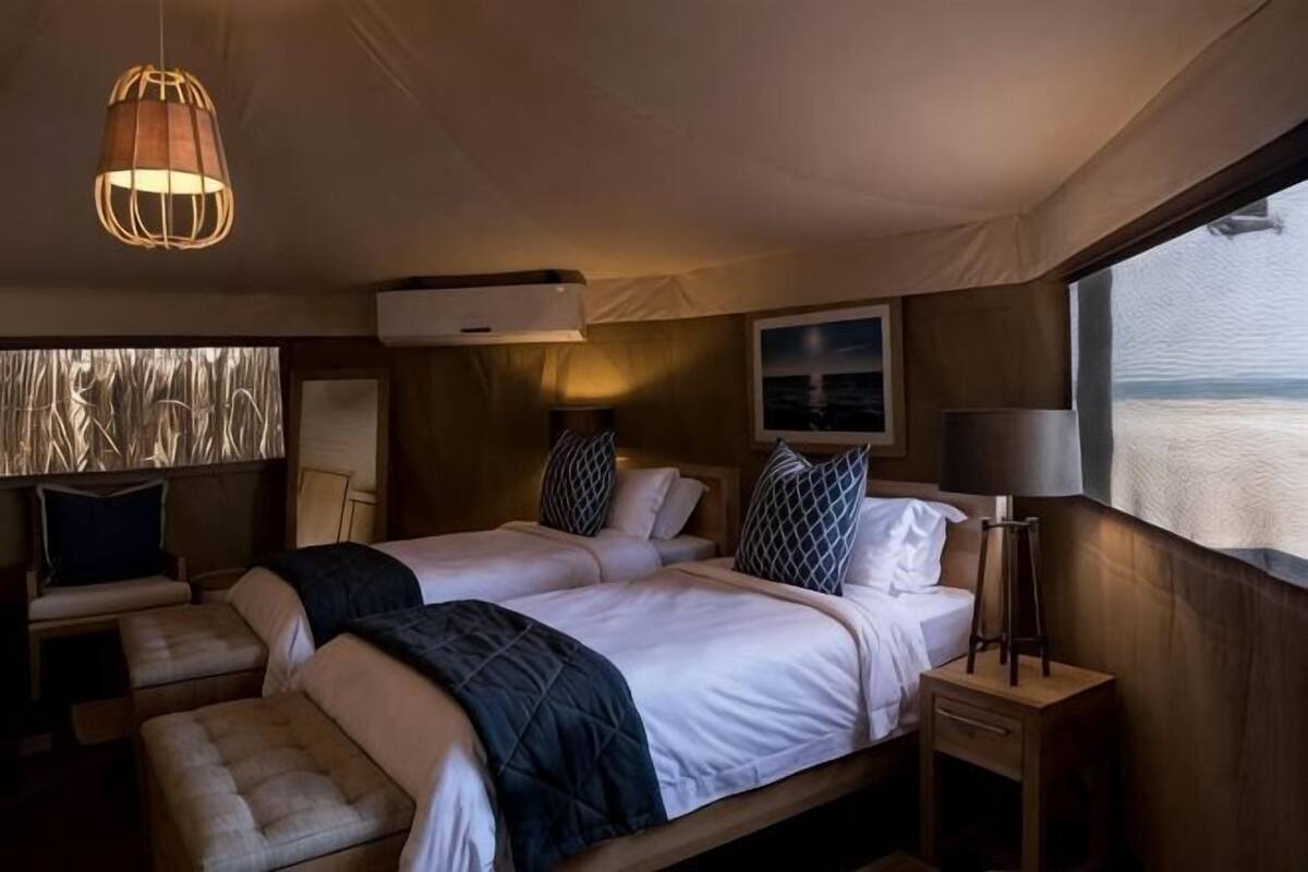 A room with two beds, a bench, a lamp, and a view of the sea.