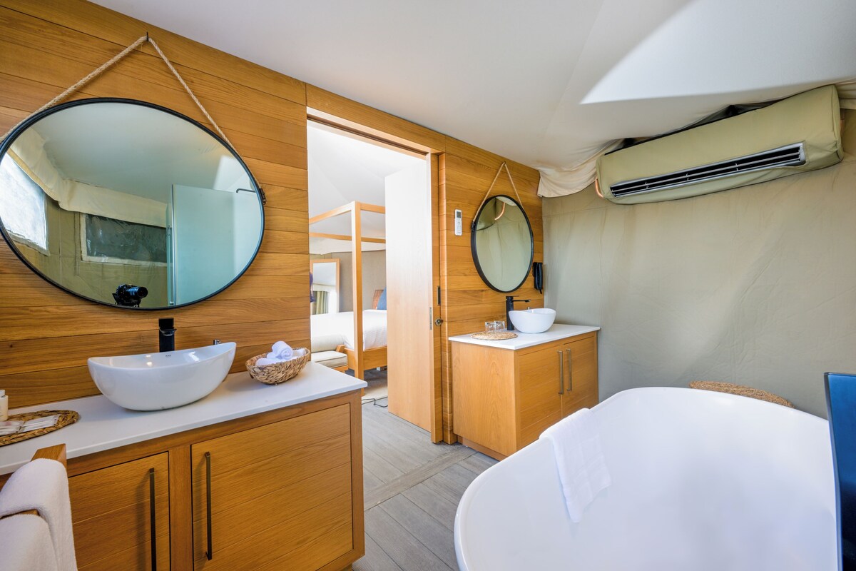 Un baño moderno con tocador de madera, un espejo redondo grande, un lavamanos blanco y una bañera.