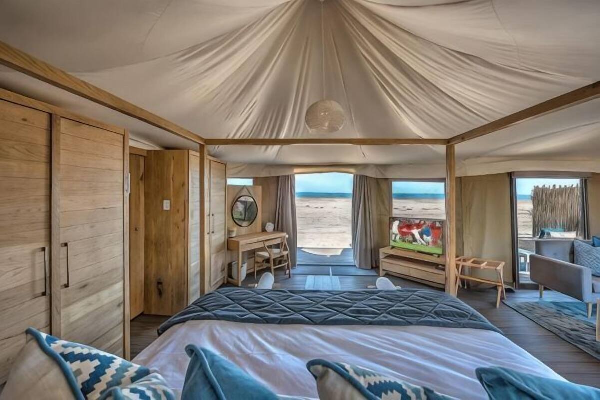 A tent-style room with a bed, a desk, and a view of the beach.