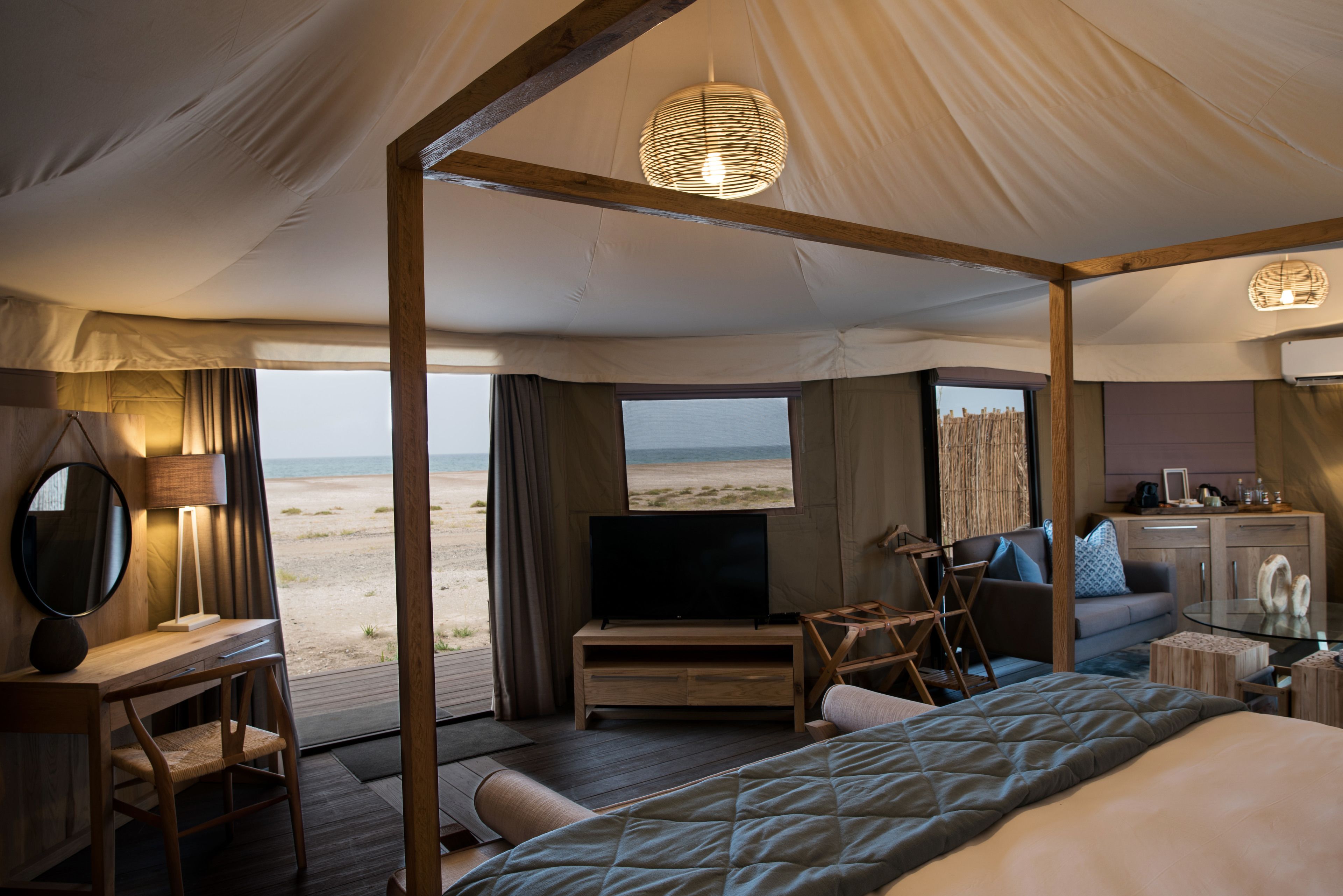 A spacious room with a large bed, a television, a desk with a lamp, and a view of the beach.