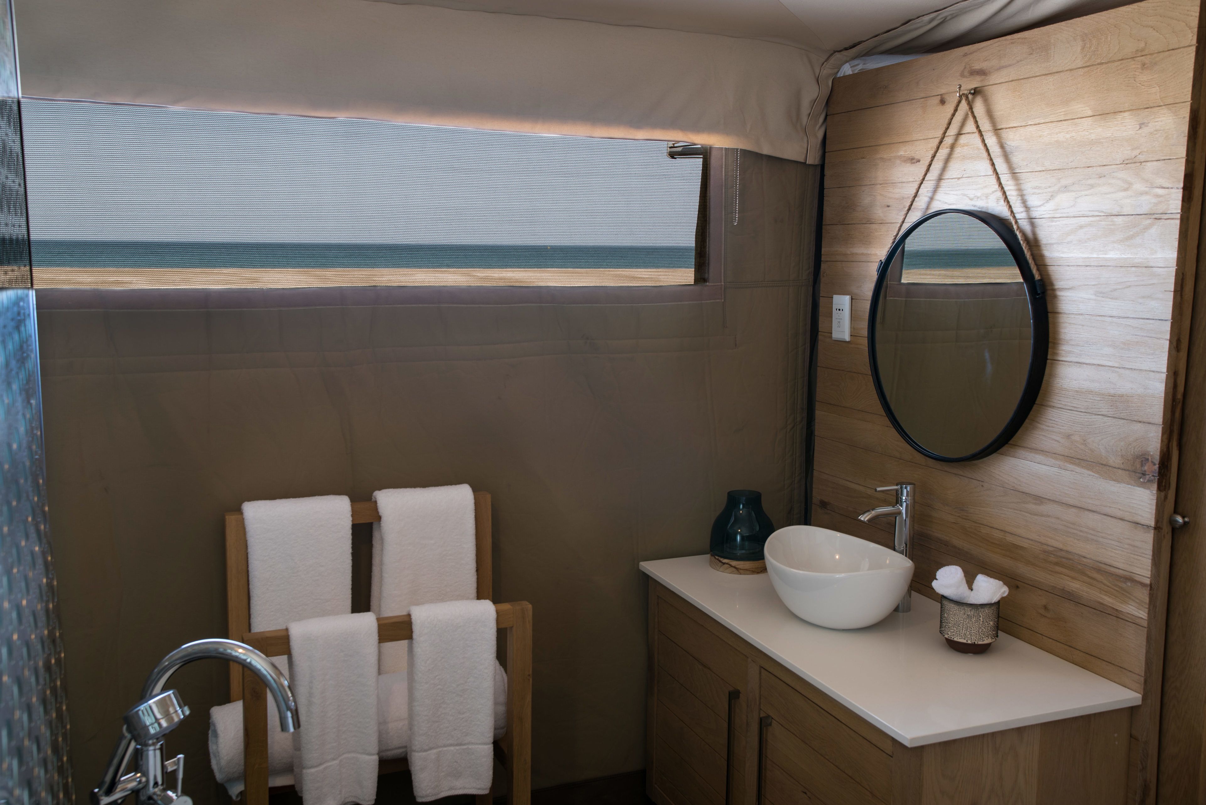 A bathroom with a wooden vanity, a white sink, a mirror, and a view of the beach through a window.