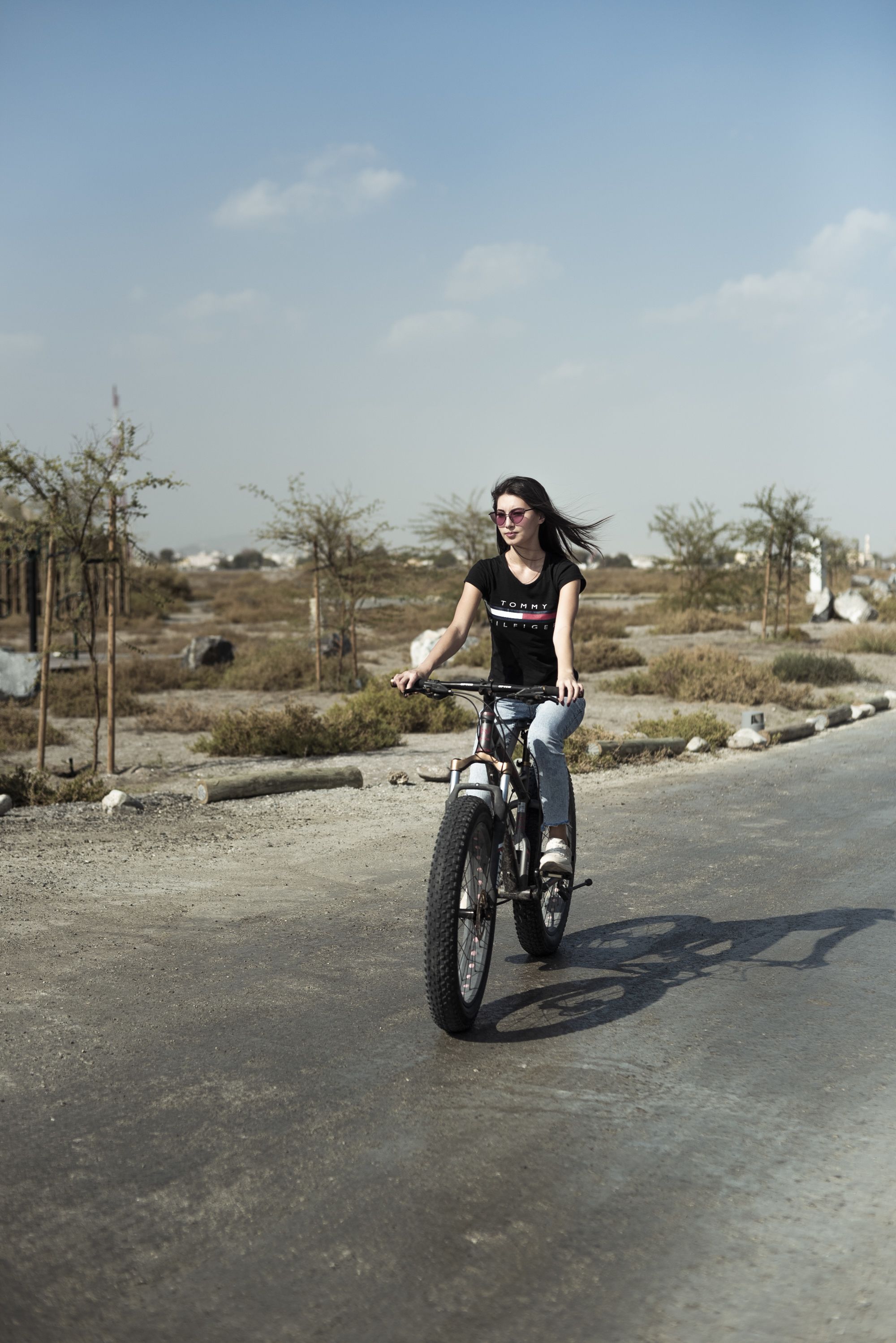 A person riding a motorcycle on a paved road with sparse vegetation and a clear sky in the background.