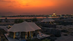 A desert resort with two tents, a pool, and a view of a city skyline at sunset.